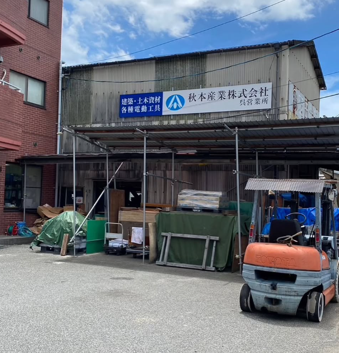 秋本産業の店舗外観。フォークリフトを備えた資材置き場と看板